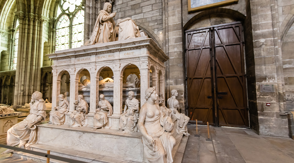 A monumental stone tomb in a cathedral. Various sculptures of figures adorn the outside of the tomb.